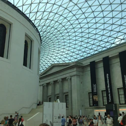 Insidan av en stor byggnad med ett glastak, vita väggar, banderoller och en folkmassa som går och minglar.