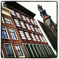 Tippad vy över tegelbyggnader med stora fönster bredvid ett kyrktorn med en klocka och ett blått och rött emblem.