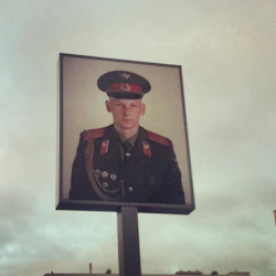 Stor utomhusskylt med ett fotografi av en uniformerad man i militärdräkt, mot en molnig himmel.