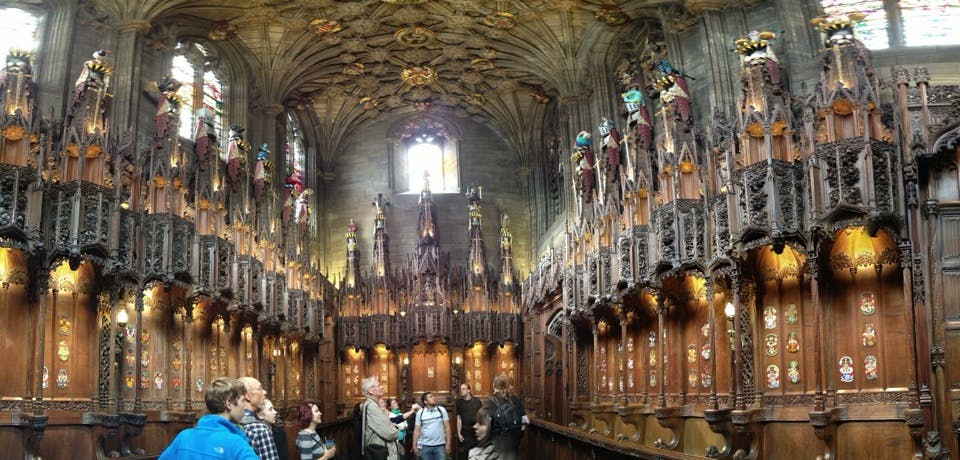 Besökare i ett stort, utsmyckat inrett rum med högt i tak, glasmålningar och invecklade träsniderier.