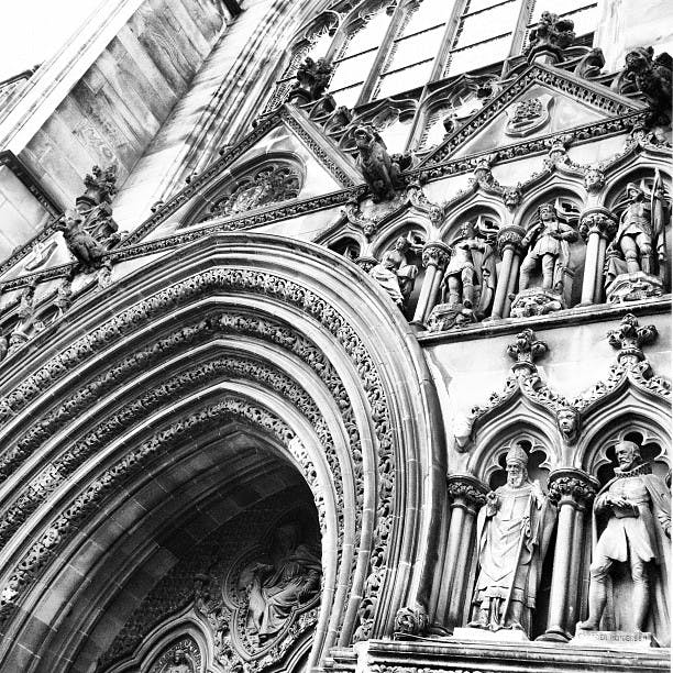 Gotisk arkitektonisk fasad med invecklade valv, skulpturer och utsmyckade sniderier under stora fönster.