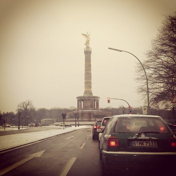 Bilar stannade vid ett trafikljus, mot segerkolonnen med sin gyllene staty, en snöig mulen dag.