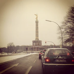 Bilar stannade vid ett trafikljus, mot segerkolonnen med sin gyllene staty, en snöig mulen dag.