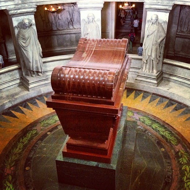 En stor rødbrun sarkofag sidder centralt i en rotunde omgivet af marmorstatuer.