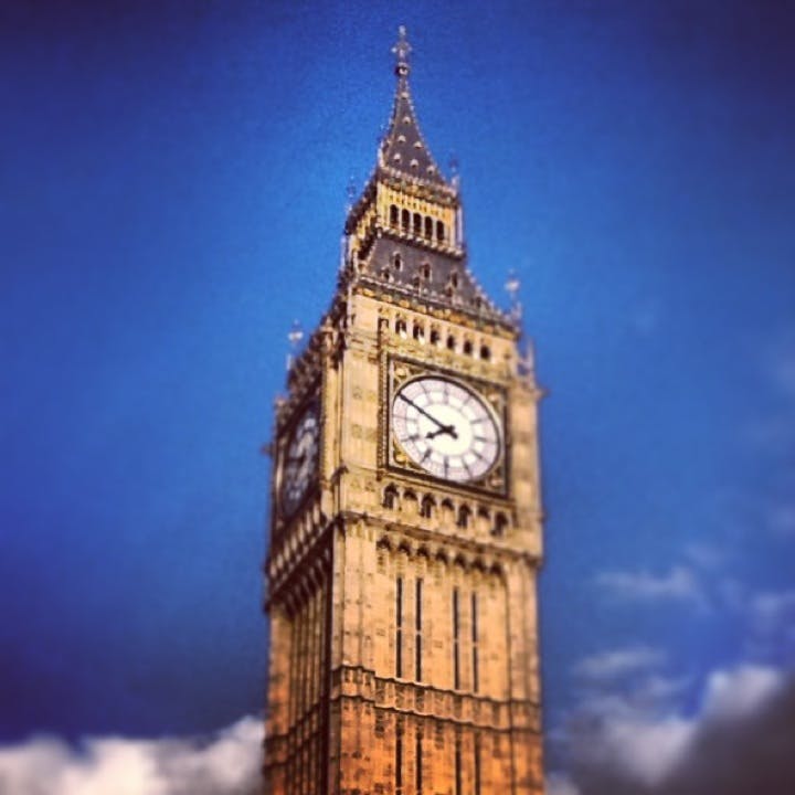 En närbild av klocktornet som visar två urtavlor mot en klarblå himmel.