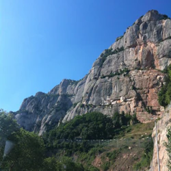 En slingrande väg intill en skir bergssida med utspridd grönska och en klarblå himmel ovanför.