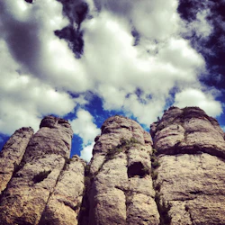 Höga, ojämna klippformationer med grön vegetation under en ljus himmel fylld av spridda vita moln.