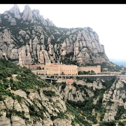 Ett stort byggnadskomplex inbäddat bland robusta, steniga berg med grönska utspridda överallt.