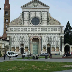 Utsmyckad, symmetrisk vit marmorkyrkofasad med gröna accenter, högt klocktorn till vänster och grön gräsmatta med människor framför.