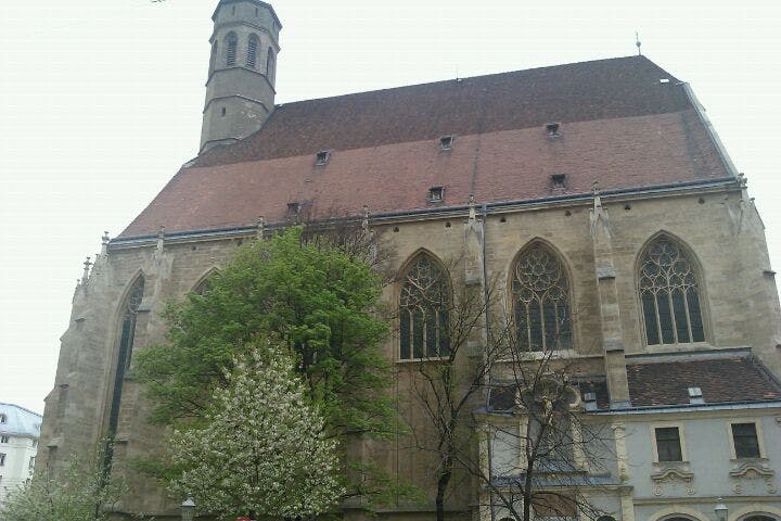 En historisk kyrka med gotiska fönster och ett högt torn, delvis skymt av träd.