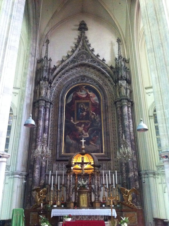 Genomarbetat altare i en gotisk kyrka med en stor målning, många ljus, ett krucifix och dekorativa guldelement.