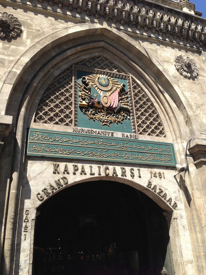 Arco de entrada para o Grande Bazar em Istambul, com esculturas intrincadas, um brasão e escrita árabe. A placa indica "Kapalıçarşı 1461".
