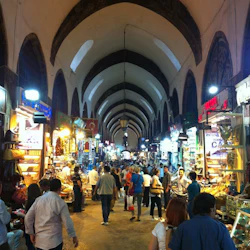 Trångt inomhusmarknad med välvda tak och många starkt upplysta bås som säljer en mängd olika varor och människor som handlar.