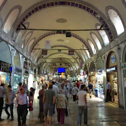 Människor som går genom en livlig marknadsplats med välvda tak med olika butiker, inklusive smyckes- och klädbutiker, på båda sidor.