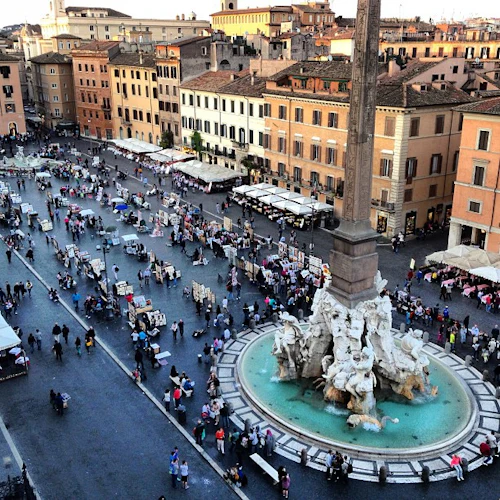 Busy square med en utsmyckad fontän i mitten, omgiven av marknadsstånd och människor, förbisedd av höga byggnader.