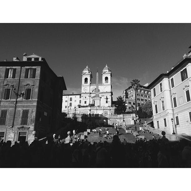 Svartvitt foto av Spanska trappan i Rom, trångt med människor, med Trinità dei Monti-kyrkan och byggnader i bakgrunden.