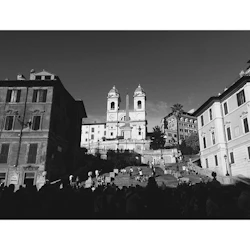 Svartvitt foto av Spanska trappan i Rom, trångt med människor, med Trinità dei Monti-kyrkan och byggnader i bakgrunden.