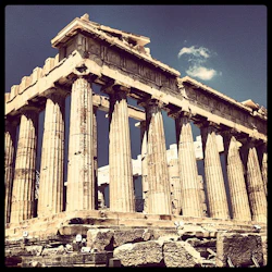 Forntida grekiska tempelruiner med doriska pelare och ett delvis kollapsat tak, under en klar himmel med ett litet moln.