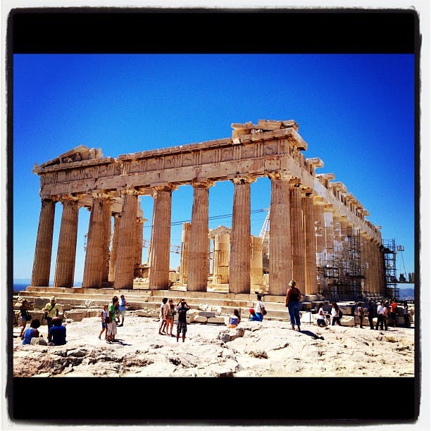 Turister som besöker det antika Parthenon-templet i Aten, Grekland, under en klarblå himmel med byggnadsställningar synliga för restaurering.