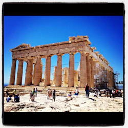 Turister som besöker det antika Parthenon-templet i Aten, Grekland, under en klarblå himmel med byggnadsställningar synliga för restaurering.