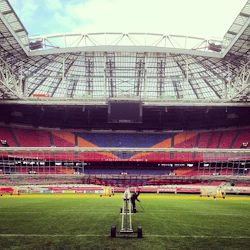 En arbetare tenderar att gå på fältet under det öppna taket på en stor, tom stadion med färgglada sittplatser och en stor skärm.