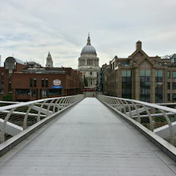 En vy nerför en gångbro mot en välvd byggnad med modern och historisk arkitektur på vardera sidan.