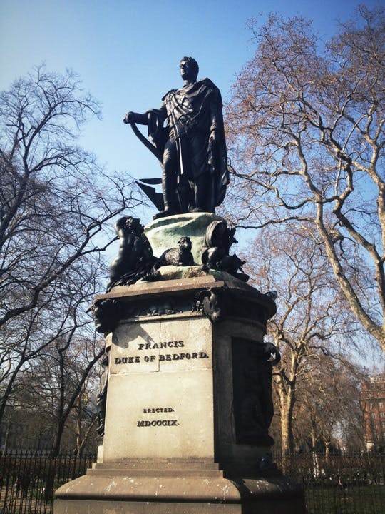 Staty av Francis, hertig av Bedford, omgiven av lövlösa träd på en klar dag. Basinskriptionen lyder "MDCCCX:IX."