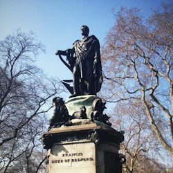 Staty av Francis, hertig av Bedford, omgiven av lövlösa träd på en klar dag. Basinskriptionen lyder "MDCCCX:IX."