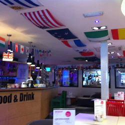 Caféinteriör dekorerad med internationella flaggor, en bänk med "SHA Food & Drink" -skylt och sittplatser med färgglada stolar.