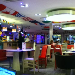 Ett ljust upplyst café med internationella flaggor som hänger från taket, färgglada stolar och människor som sitter vid borden.