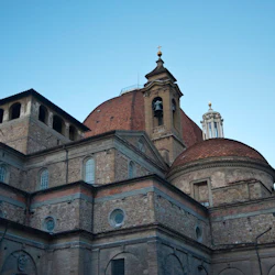 Stenkyrka med välvda fönster, välvda tak och ett klocktorn under en klar himmel.