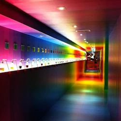 En lång hall med färgglad regnbågsbelysning, numrerade displayer och små behållare på vänster vägg, vilket leder till en speglad ände.