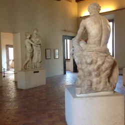 Ett museumrum har klassiska statyer: en av en sittande figur, en annan av två stående figurer som omfamnar, mitt i naturligt ljus.