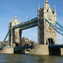 Tower Bridge sträcker sig över floden med två stora torn, upphängningskablar och byggnader i bakgrunden på en klar dag.