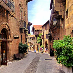 Smal gågata med historiska byggnader, hängande lyktor och balkonger. Flera personer går nära byggnaderna.